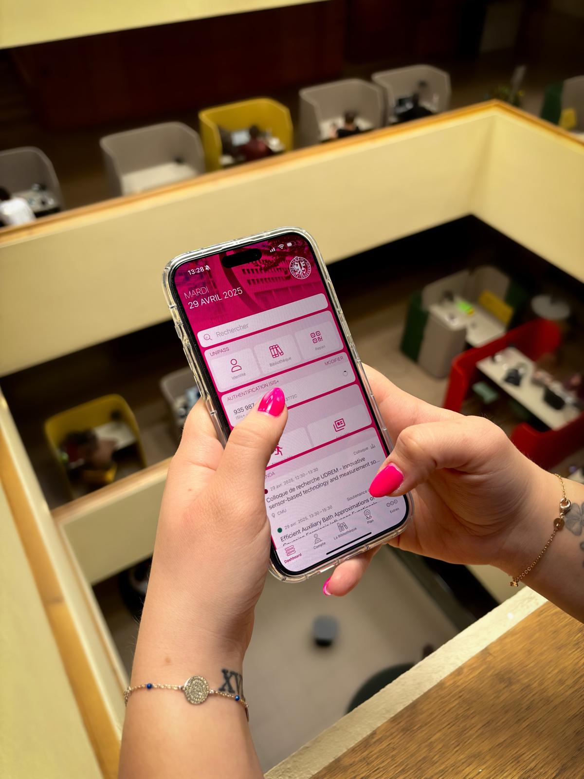 Image décorative d’une personne aux ongles vernis roses qui tient un téléphone portable où s’affiche l’application mobile UNIGE.